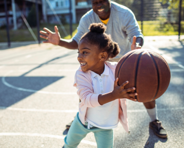 Girl and her dad playing basketball.